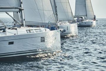 Naklejka premium Sailboats compete in a sailing regatta at sunset, sailing race, reflection of sails on water, white color of sails, boat number aft boats