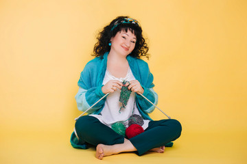 A beautiful and smiling woman of fifty years old on a yellow background knits yarn. Sits on the...