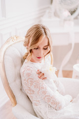 Naklejka premium Beautiful bride in a white laced dress and wedding bouquet is preparing for wedding ceremony in hotel room. Bride getting ready. Artwork
