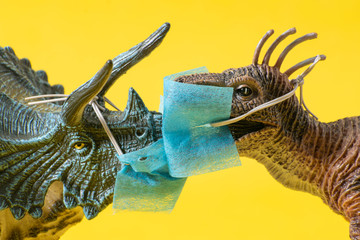 Two plastic dinosaur toys with face masks kissing on  yellow background