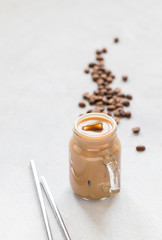 Obraz na płótnie Canvas Iced coffee milk in a jar with a metal tube on a light gray background