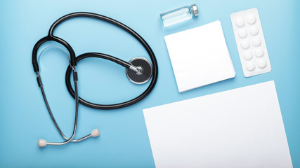 Medical concept. Flat lay stethoscope, pills, Ampoule, pen and stickers, white blank sheet of paper on a blue background with copy space. Mockup