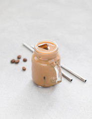 Cold coffee with milk and ice in a jar on a light background 