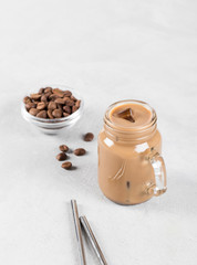 Coffee milk with ice in a jar with a metal tube on a white background