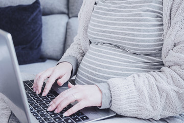 Naklejka premium Young pregnant woman working at home with her laptop