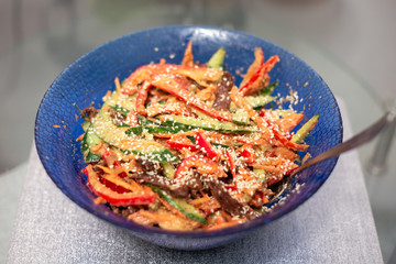 vegetable salad with meat, sprinkled with sesame seeds, in a blue salad bowl, blurred background, delicious lunch at home