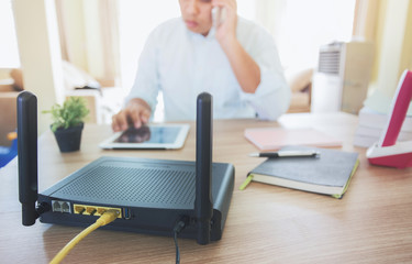 closeup of a wireless router and a man using smartphone on living room at home ofiice, equipment...