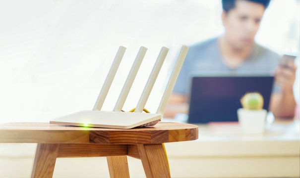 closeup of a wireless router and a man using smartphone on living room at home ofiice, equipment for  working from home, while in quarantine isolation during the Covid-19 health crisis.