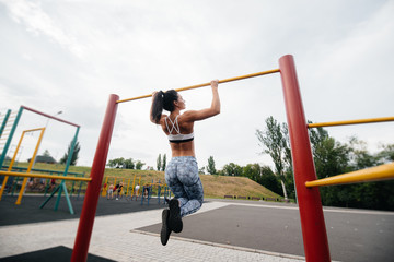 Fototapeta premium Sexy girl is pulled up on a horizontal bar in the open air. Fitness. Healthy lifestyle