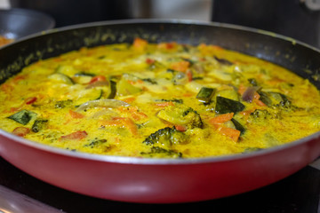 delicious yellow curry with vegetables and coconut milk in a red and black frying pan