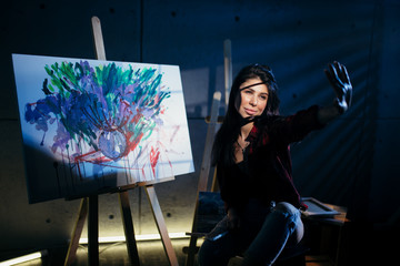 Beautiful brunette girl artist sitting in a dark Studio near the easel with painted watercolor...