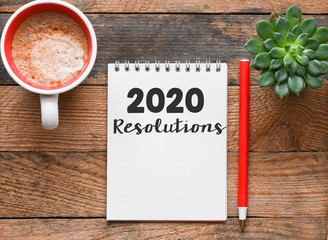2020 resolutions text on notepad with computer on office background. Business concept.