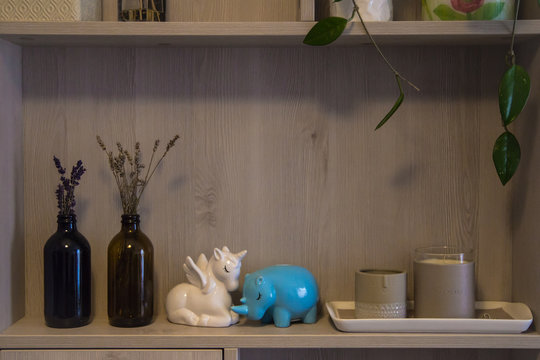 Decorations for the house stood on a shelf of the cupboard (bottles with dried flowers, piggy banks in the form of a white rhino and blue unicorn, candle-sticks) in warm beige colors.	