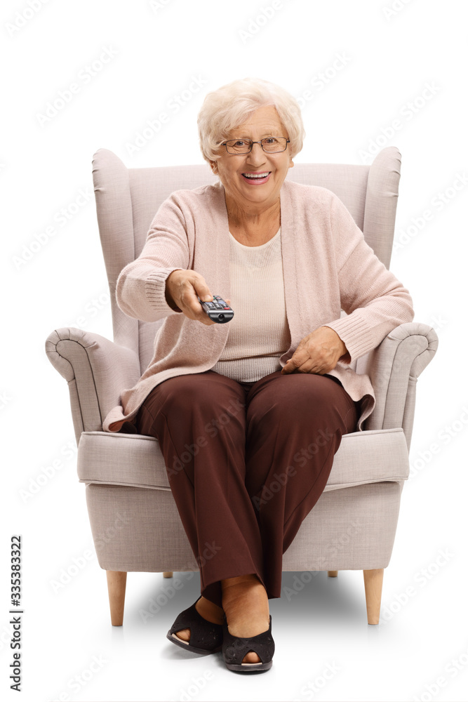 Wall mural Senior woman sitting in an armchair and holdin a tv remote control