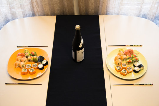 A table for two with a sushi maki set and a bottle of sake in a minimalist style and warm colors.