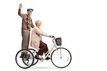 Senior man waving from a tricycle and senior woman riding
