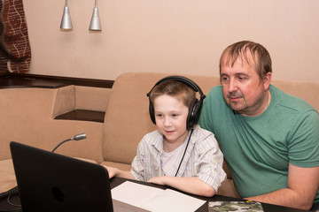 Obraz premium Dad and son and the Maine Coon cat are sitting at a table on the sofa and watching a video lesson on a laptop. Home distance learning online. Quarantine.