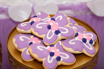 Cookies in shape of a butterfly decorated with purple icing and presented on a golden plate.