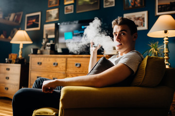 Exhaling the vapor with electronic cigarette.Puffing clouds of smoke.Vape flavor liquid chemicals.Use of e-cigarettes in the home.Smoking and vaping negative health effects.Nicotine addiction habit
