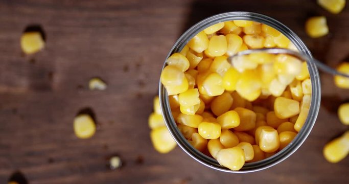 Man's hand with a spoon mixes canned corn in a tin.