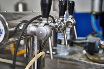 Metallic taps with black rubber handles in a row connected to machines in a brewery