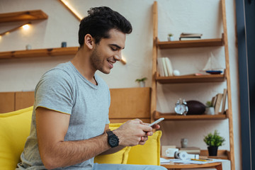 Man chatting on smartphone and smiling on sofa in living room