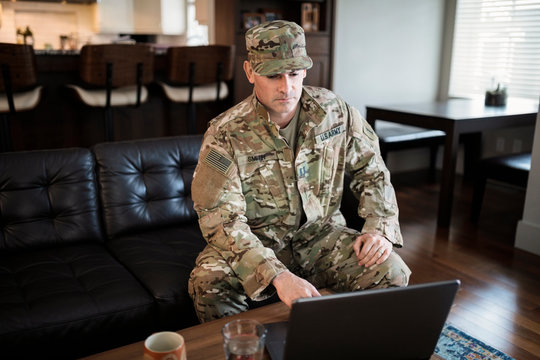 Male soldier in camouflage uniform using laptop in living room