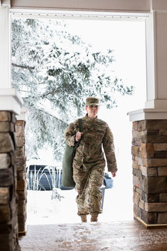 Female Soldier In Camouflage Returning Home On Snowy House Porch