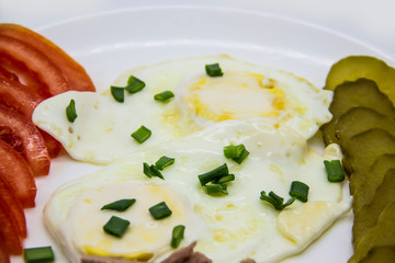 Delicious fresh tuna with eggs, tomatoes, cucmbers with green onion at the morning. Healthy and diet breakfast with tuna, eggs and vegetables on the white plate against white background