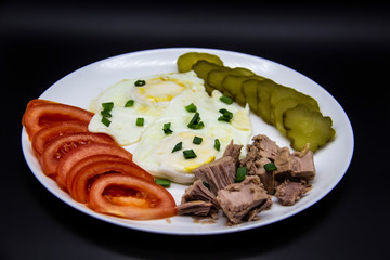 Delicious fresh tuna with eggs, tomatoes, cucmbers with green onion at the morning. Healthy and diet breakfast with tuna, eggs and vegetables on the white plate against dark background