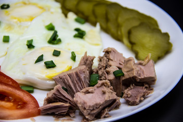 Delicious fresh tuna with eggs, tomatoes, cucmbers with green onion at the morning. Healthy and diet breakfast with tuna, eggs and vegetables on the white plate against white background