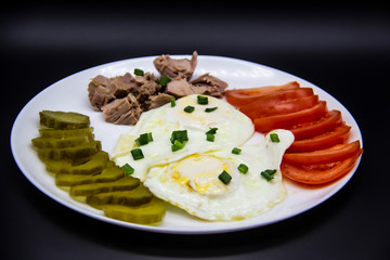 Delicious fresh tuna with eggs, tomatoes, cucmbers with green onion at the morning. Healthy and diet breakfast with tuna, eggs and vegetables on the white plate against dark background
