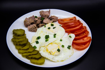 Delicious fresh tuna with eggs, tomatoes, cucmbers with green onion at the morning. Healthy and diet breakfast with tuna, eggs and vegetables on the white plate against dark background