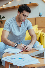 Selective focus of freelancer writing in notebook at coffee table on sofa