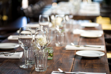 Glasses, flowers, fork, knife served for dinner in restaurant with cozy interior, retro film filter effect