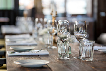 Glasses, flowers, fork, knife served for dinner in restaurant with cozy interior, retro film filter effect