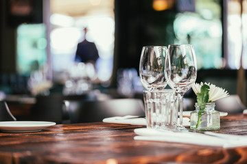 Glasses, flowers, fork, knife served for dinner in restaurant with cozy interior, retro film filter effect