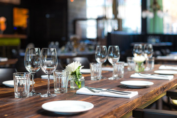 Glasses, flowers, fork, knife served for dinner in restaurant with cozy interior, retro film filter effect