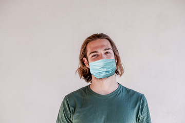 Blonde young guy wearing surgical face mask, long hair man take a face mask for coronavirus or COVID-19 epidemic