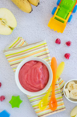 Baby food. Homemade apple puree or sauce with banana and raspberries in a bowl with a spoon on a light background. Healthy food. Vertical orientation. Top view.