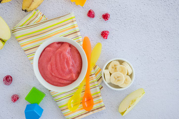 Baby food. Homemade apple puree or sauce with banana and raspberries in a bowl with a spoon on a light background. Healthy food. Horizontal orientation. Top view. Copy space.