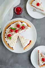 Tart with cherry filling and Italian meringue with a cocktail cherry, chocolate and mint on top on a white plate on a dark concrete background. Cherry pie. Vertical orientation, Top view.