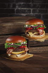 two juicy appetizing beautifully laid out hamburgers on a wooden box with crispy bacon, cheese,...
