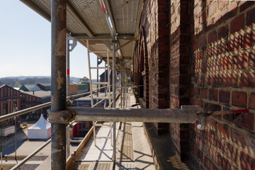 Diminishing perspective view and selected focus at the inner of scaffolds in front of old historical building with beautiful brick decorative facade and windows at renovated construction site.