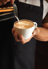 Hands of a barista pouring warm milk into a cappuccino or latte making a pattern of milk into coffee. Barista work