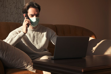 Single male with medical mask, sitting at home and have chat on his mobile