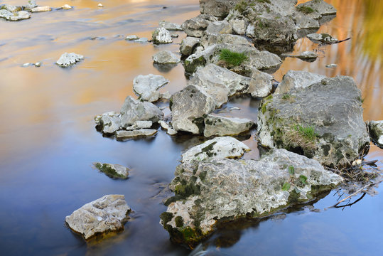 Calm atmospheric picture of large stones lying in a river in the evening, around which the water flows very calmly and which form a path