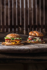 two burgers appetizing bun with sesame seeds, meat, cheese, sauce on a wooden table and parchment, ready poster for printing