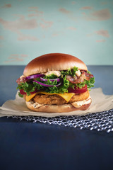 hamburger with crispy bacon, lettuce, chicken cutlet and cheese on a metal grill and parchment