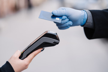 Faceless human in medical gloves during coronavirus epidemic, holds plastic card, tries to makes cashless payment for safety, uses modern technology. Pandemic, virus and prevention concept